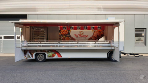 Zijaanzicht van een aanhangwagen voor kipspecialiteiten met geopende luifel en zijborden