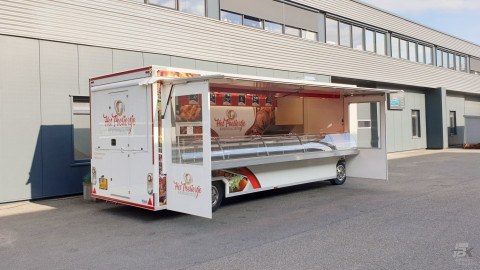 Zijaanzicht van een aanhangwagen voor kipspecialiteiten met geopende luifel en zijborden