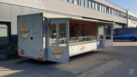 Zijaanzicht van een aanhangwagen voor kaas met geopende luifel en zijborden