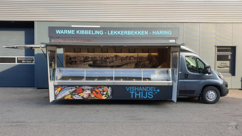 Zijaanzicht van een verkoopwagen voor vis met geopende luifel en zijborden