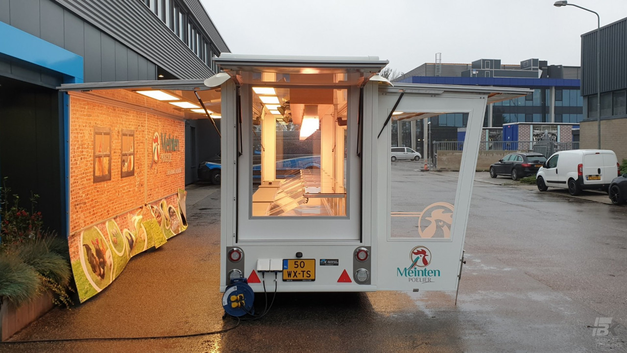Achteraanzicht van een smalle aanhangwagen voor kip met geopende luifel en zijborden