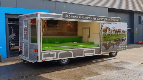 Zijaanzicht van een verkoopwagen voor kaas met geopende luifel en zijbord