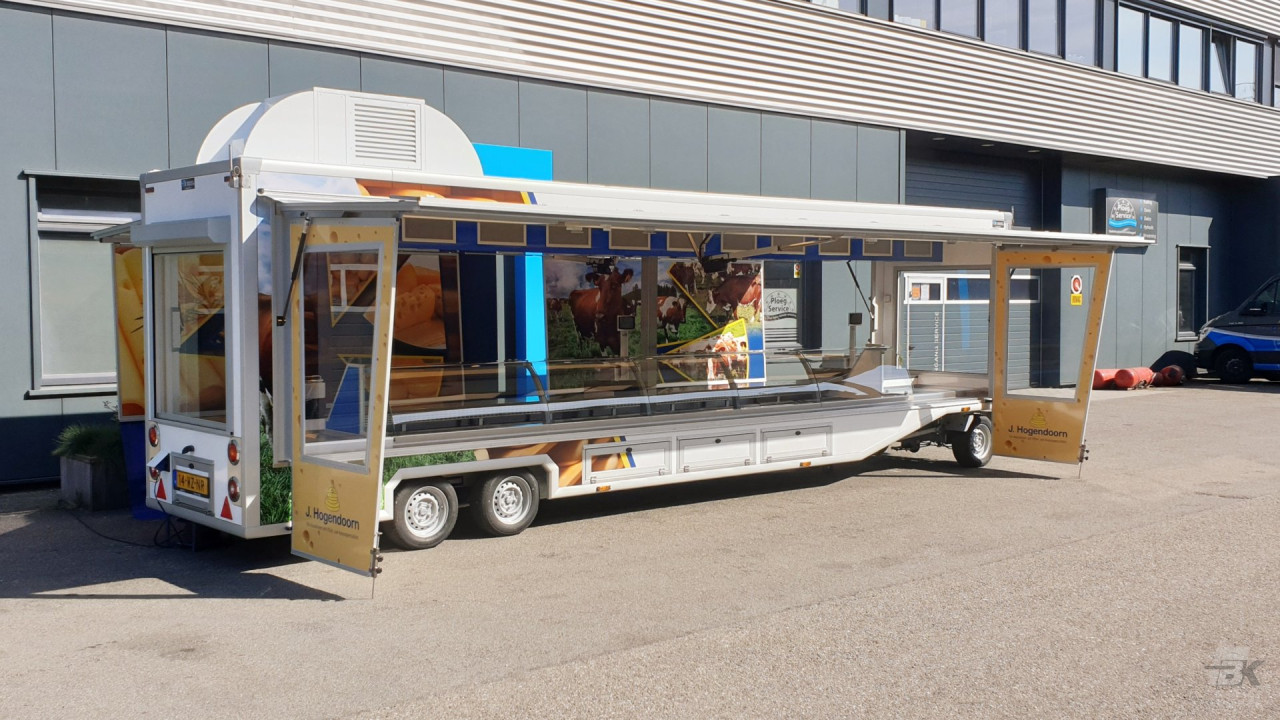 Zijaanzicht van een smalle aanhangwagen voor kaas met geopende luifel en zijborden