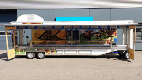 Zijaanzicht van een smalle aanhangwagen voor kaas met geopende luifel en zijborden