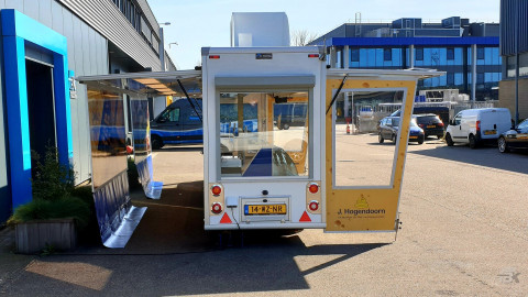 Achteraanzicht van een smalle aanhangwagen voor kaas met geopende luifel en zijborden