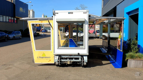 Vooraanzicht van een smalle aanhangwagen voor kaas met geopende luifel en zijborden