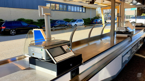 Binnenkant van een smalle aanhangwagen voor kaas met toonbank, vitrine en kassa