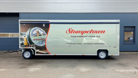 Zijaanzicht van een aanhangwagen voor kaas en kipspecialiteiten met gesloten luifel