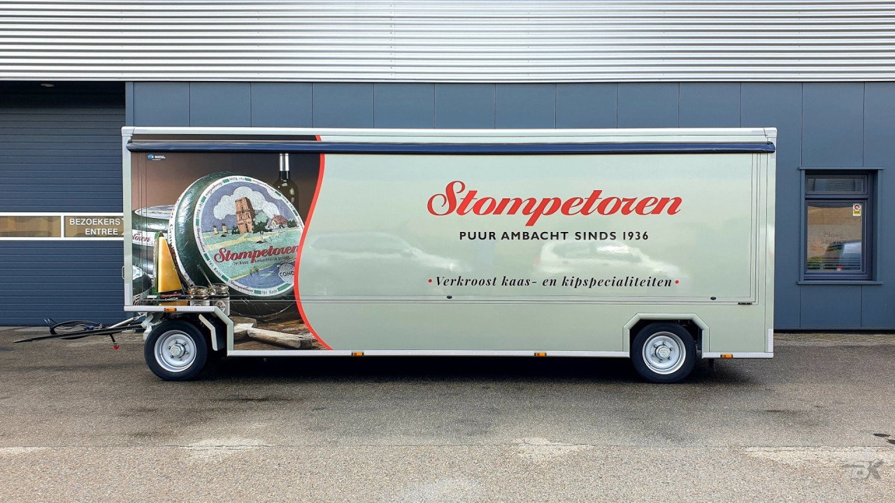 Zijaanzicht van een aanhangwagen voor kaas en kipspecialiteiten met gesloten luifel