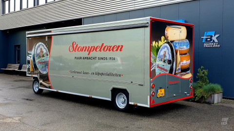 Zijaanzicht van een aanhangwagen voor kaas en kipspecialiteiten met gesloten luifel