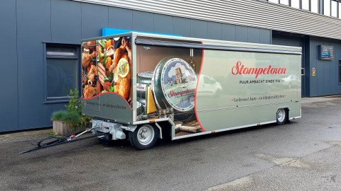 Zijaanzicht van een aanhangwagen voor kaas en kipspecialiteiten met gesloten luifel