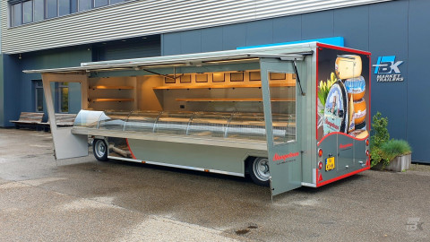 Zijaanzicht van een aanhangwagen voor kaas en kipspecialiteiten met geopende luifel en zijborden