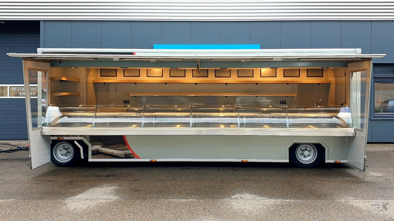 Zijaanzicht van een aanhangwagen voor kaas en kipspecialiteiten met geopende luifel en zijborden