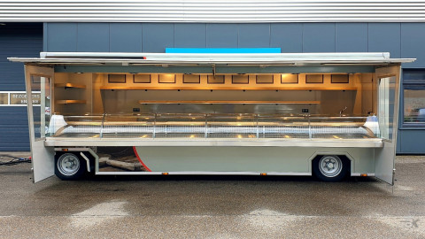 Zijaanzicht van een aanhangwagen voor kaas en kipspecialiteiten met geopende luifel en zijborden