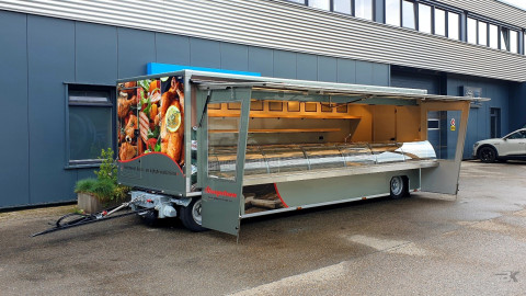 Zijaanzicht van een aanhangwagen voor kaas en kipspecialiteiten met geopende luifel en zijborden