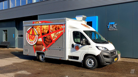 Zijaanzicht van een verkoopwagen voor loempia's, patat en snacks met gesloten luifel