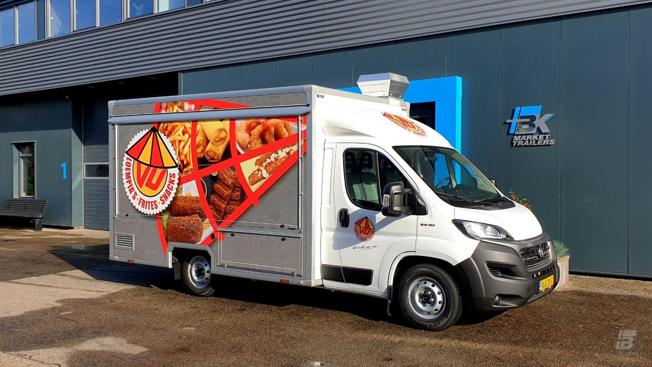 Zijaanzicht van een verkoopwagen voor loempia's, patat en snacks met gesloten luifel