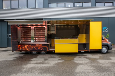 Zijaanzicht van een verkoopwagen voor kip aan het spit met geopende luifel en zijborden