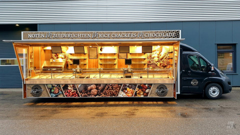 Zijaanzicht van een verkoopwagen voor noten met geopende luifel en zijborden
