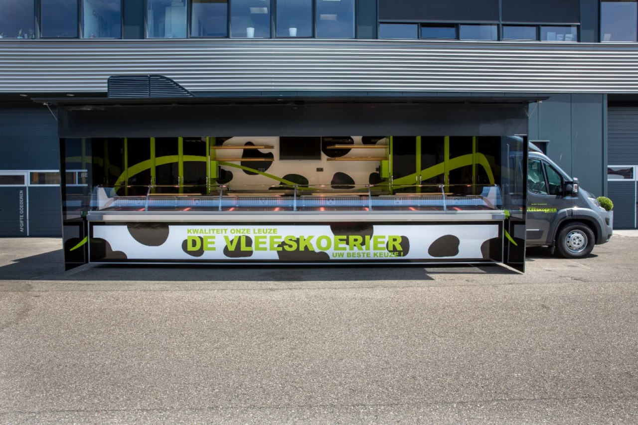 Zijaanzicht van een verkoopwagen voor vlees met geopende luifel en zijborden