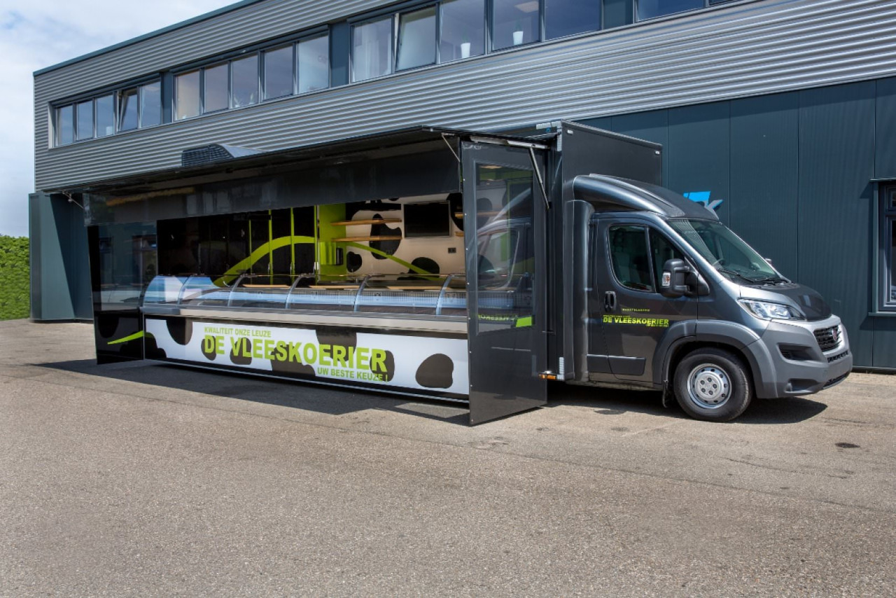 Zijaanzicht van een verkoopwagen voor vlees met geopende luifel en zijborden