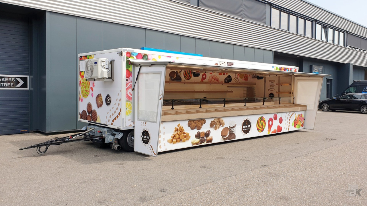 Zijaanzicht van een aanhangwagen voor drop, snoep en chocolade met geopende luifel en zijborden
