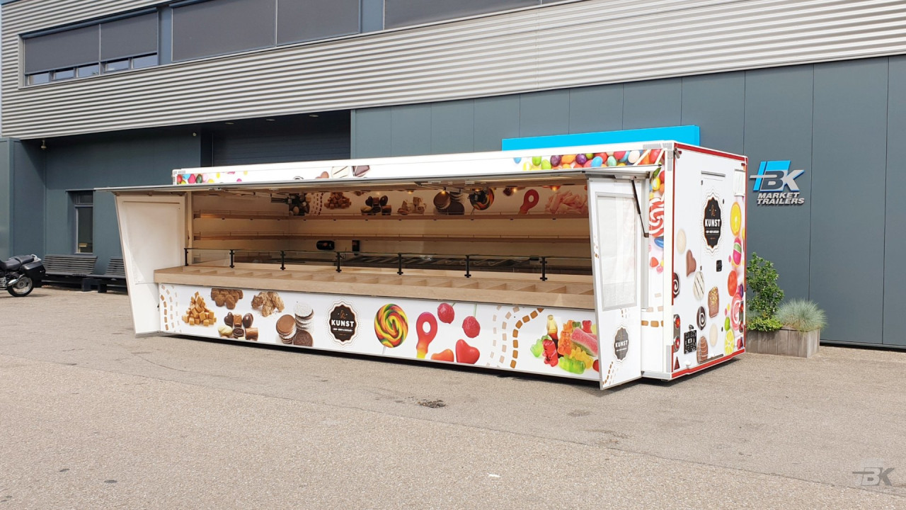 Zijaanzicht van een aanhangwagen voor drop, snoep en chocolade met geopende luifel en zijborden