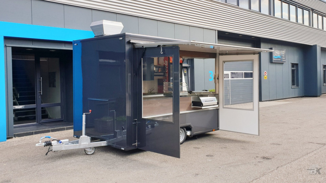 Zijaanzicht van een kleine aanhangwagen voor loempia's met geopende luifel en zijborden