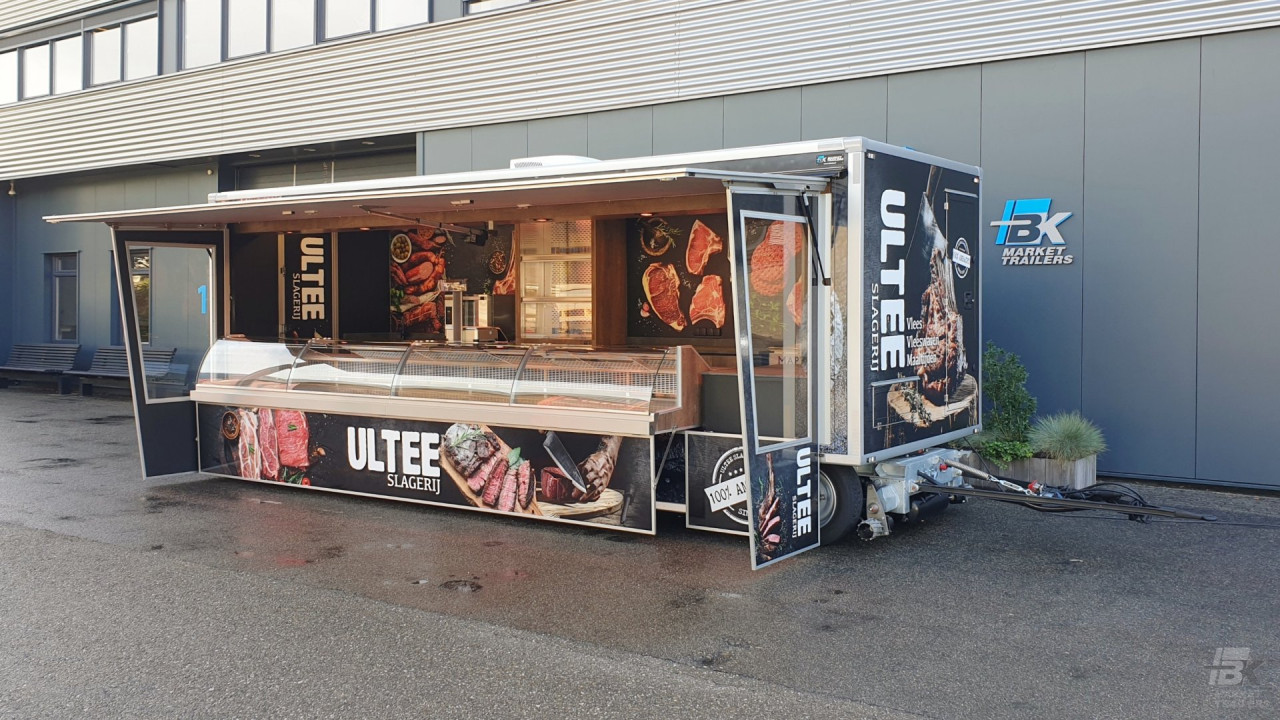 Zijaanzicht van een aanhangwagen voor vlees met geopende luifel en zijborden