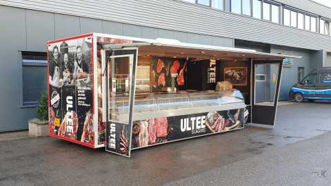 Zijaanzicht van een aanhangwagen voor vlees met geopende luifel en zijborden