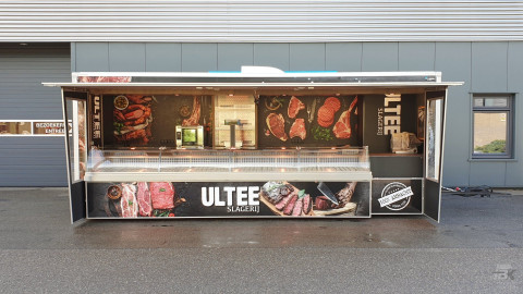 Zijaanzicht van een aanhangwagen voor vlees met geopende luifel en zijborden