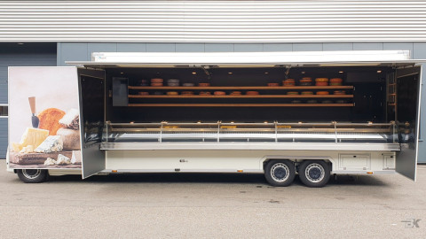 Zijaanzicht van een verkoopwagen voor kaas met geopende luifel en zijborden