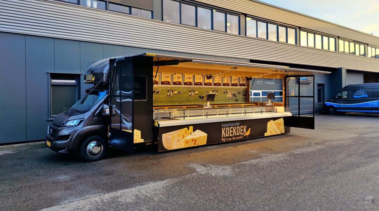 Zijaanzicht van een verkoopwagen voor kaas met geopende luifel en zijborden