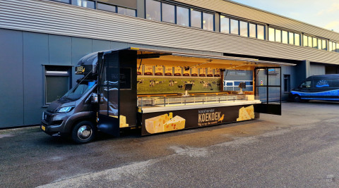 Zijaanzicht van een verkoopwagen voor kaas met geopende luifel en zijborden