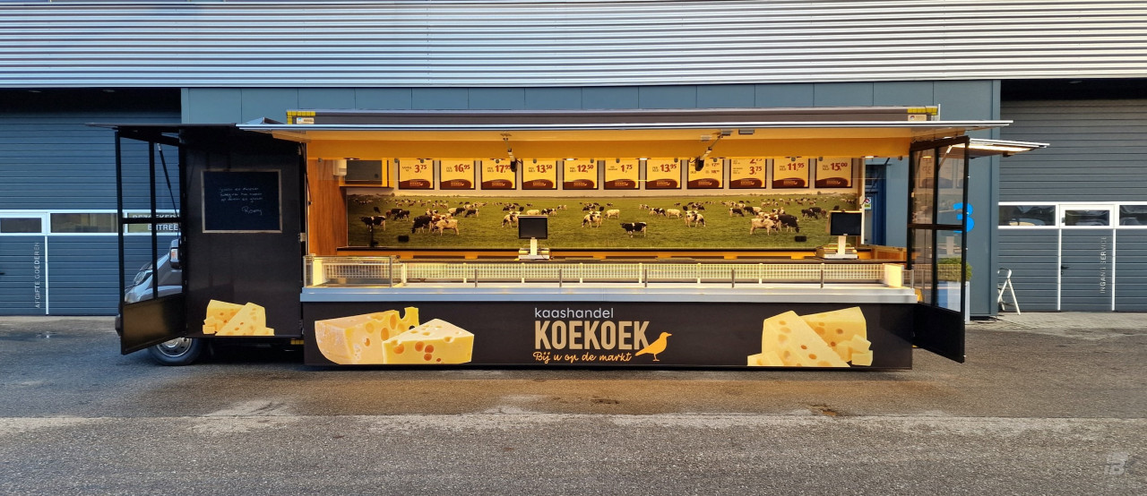 Zijaanzicht van een verkoopwagen voor kaas met geopende luifel en zijborden