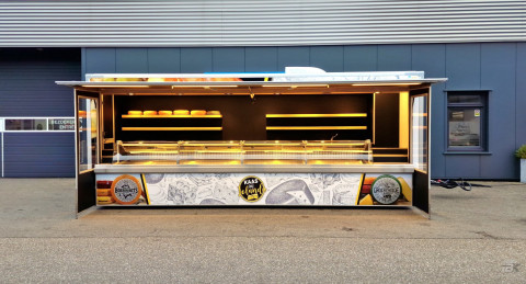 Zijaanzicht van een verkoopwagen voor kaas met geopende luifel en zijborden