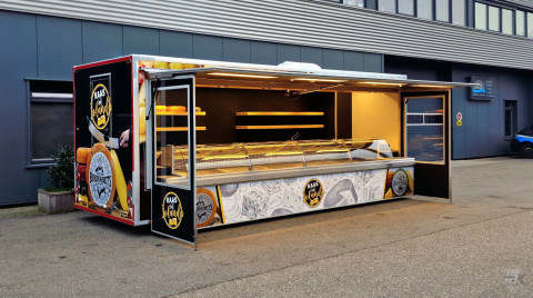 Zijaanzicht van een verkoopwagen voor kaas met geopende luifel en zijborden