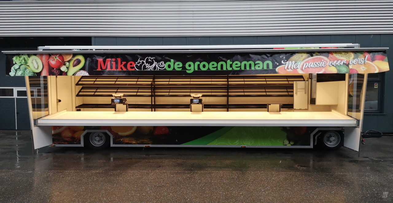 Zijaanzicht van een aanhangwagen voor groente en fruit met geopende luifel en zijborden