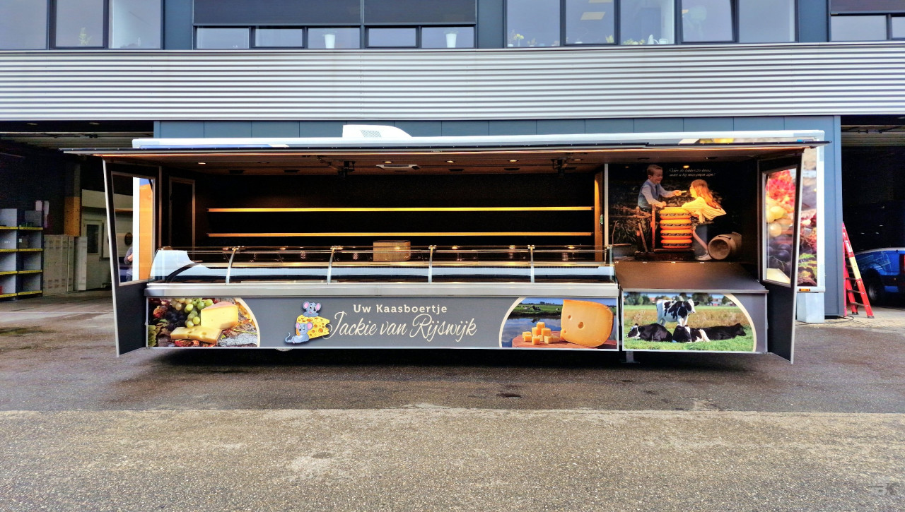 Zijaanzicht van een verkoopwagen oplegger voor kaas met geopende luifel en zijborden