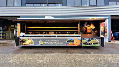 Zijaanzicht van een verkoopwagen oplegger voor kaas met geopende luifel en zijborden