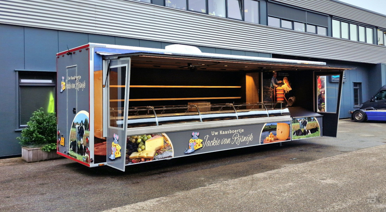 Zijaanzicht van een verkoopwagen oplegger voor kaas met geopende luifel en zijborden