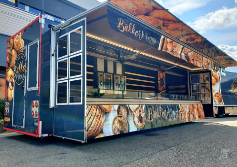 Zijaanzicht van een verkoopwagen voor brood en banket met geopende luifel en zijborden