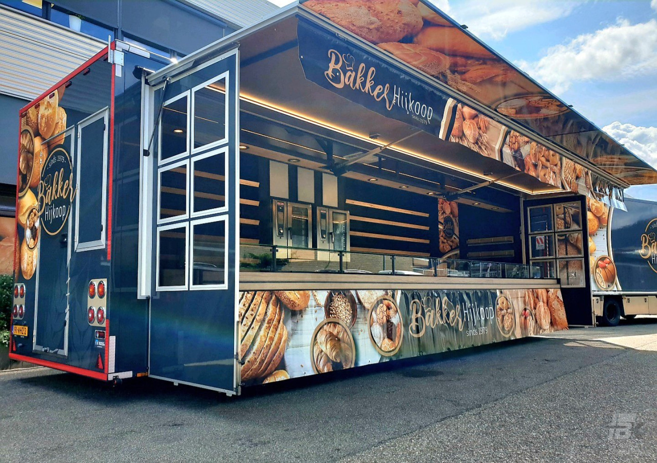 Zijaanzicht van een verkoopwagen voor brood en banket met geopende luifel en zijborden