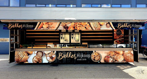 Zijaanzicht van een verkoopwagen voor brood en banket met geopende luifel en zijborden