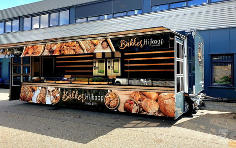 Zijaanzicht van een verkoopwagen voor brood en banket met geopende luifel en zijborden