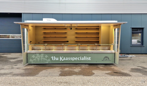 Zijaanzicht van een aanhangwagen voor kaas met geopende luifel en zijborden