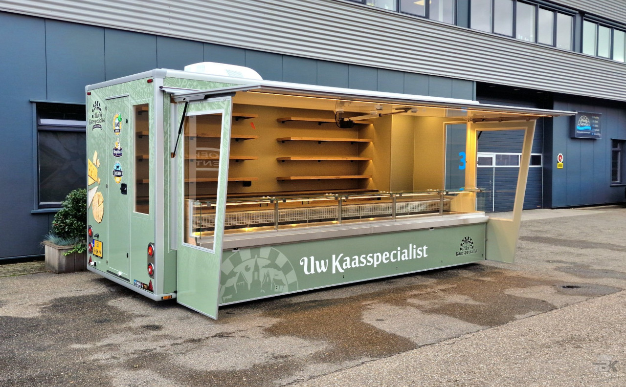 Zijaanzicht van een aanhangwagen voor kaas met geopende luifel en zijborden