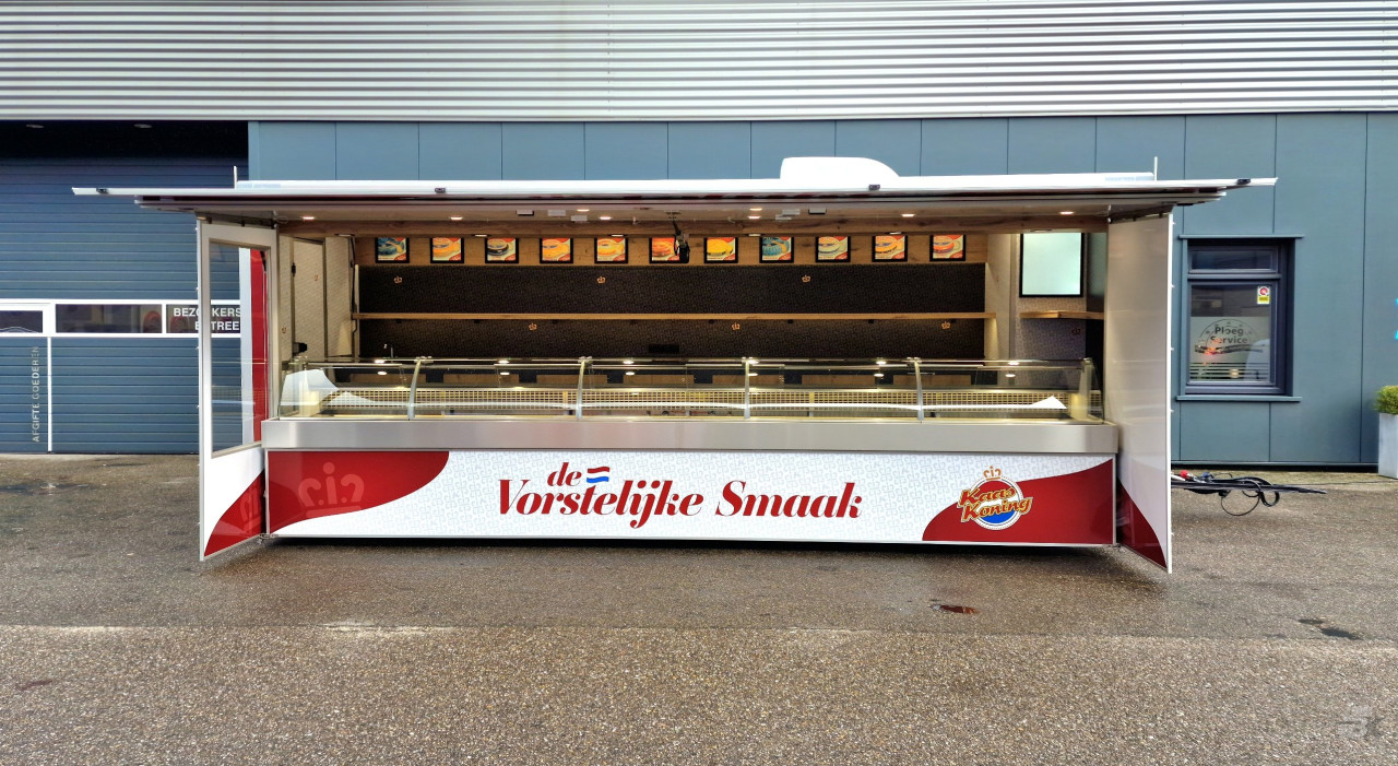 Zijaanzicht van een aanhangwagen voor kaas met geopende luifel en zijborden