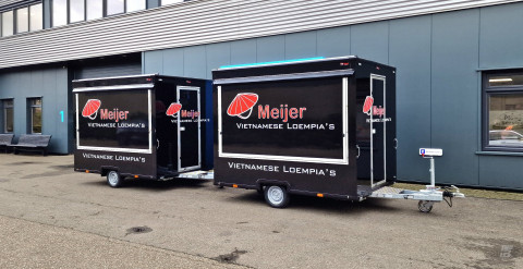 Zijaanzicht van twee kleine aanhangwagens voor loempia's met gesloten luifels