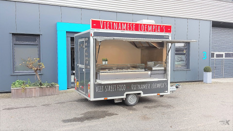 Zijaanzicht van een kleine aanhangwagen voor loempia's met geopende luifel